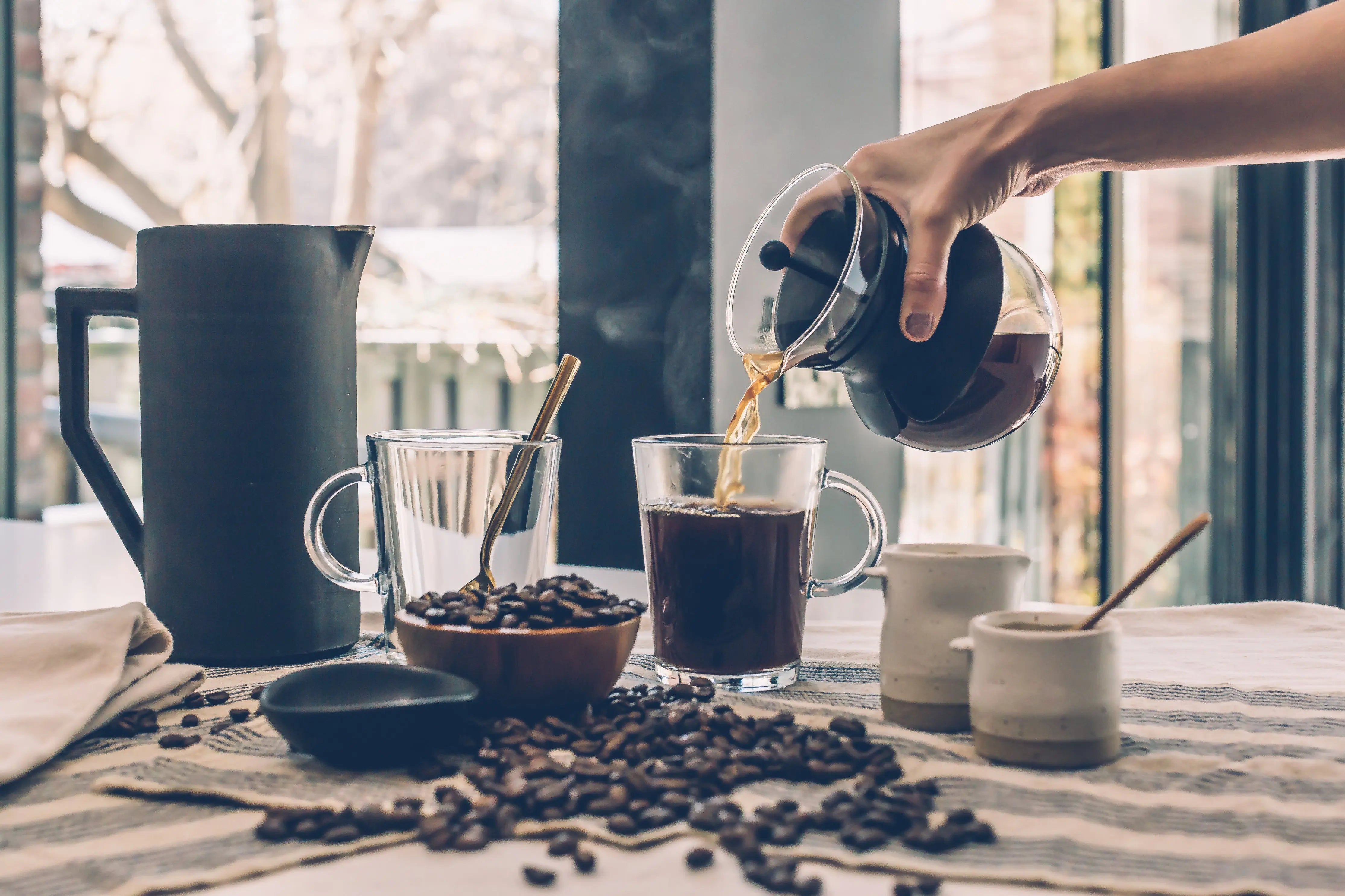 Person pouring hot coffee plus coffee beans, sugar and cream. Coffee lovers dream.