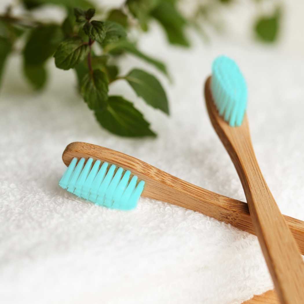 Top halves crosses  of 2 bamboo toothbrushes  wit blue bristles on a white towel with some mint leaves in the background